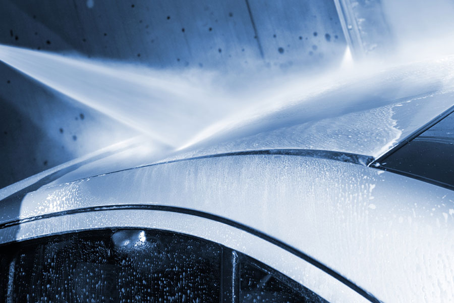 A close-up of a car roof being washed with a high-pressure water spray at a drip car wash, with water droplets and mist visible, highlighting the importance of water quality in achieving a spotless finish.