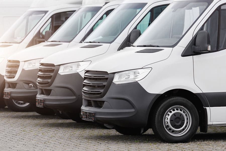 A row of white commercial vans, part of Michigan business fleets, is parked closely together on a paved lot, viewed from the front and slightly to the side—the kind of professional fleet cleaning that Drip Car Wash specializes in.